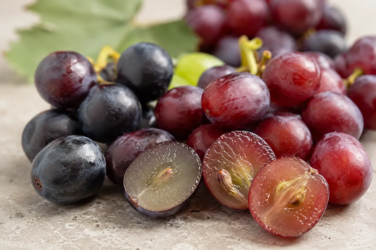 Uvas vermelhas e roxas vistas de perto, com algumas frutas cortadas mostrando a diferença entre casca e polpa.